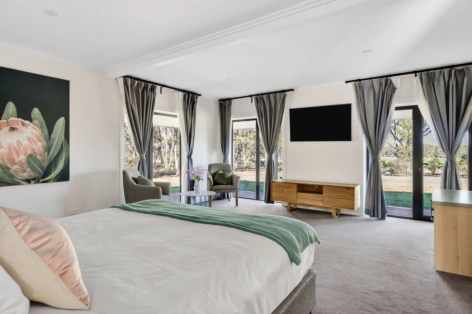 A large king suite with armchairs and glass doors on two sides looking into the bushland