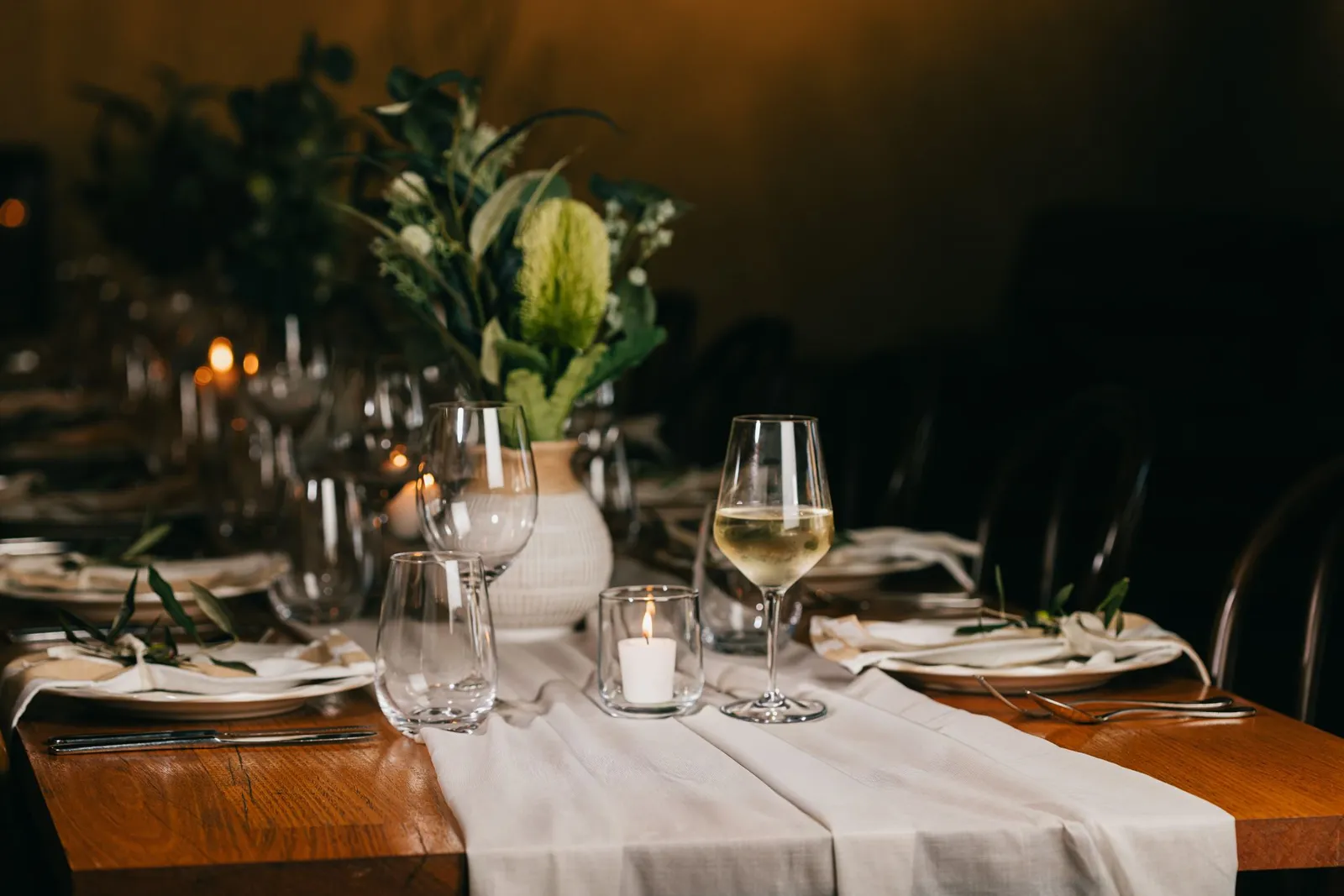 A table set for an event, candlelit, with a glass of white wine